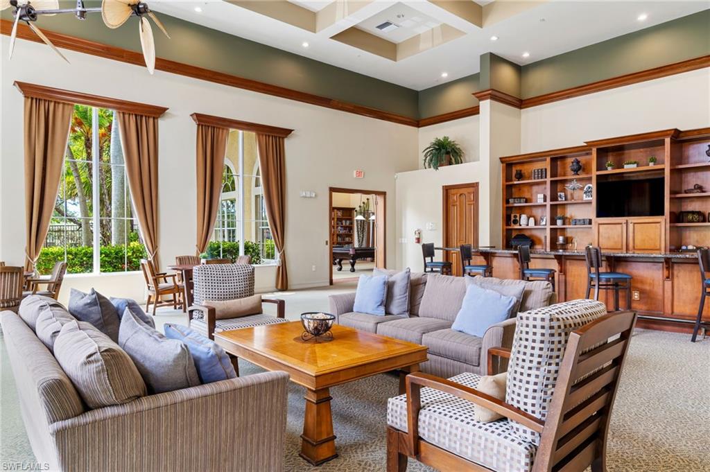 Sophisticated living room showcasing coffered ceiling detail, multiple tall windows with warm drapery, hardwood-finish flooring, and extensive built-in cabinetry with shelving and integrated media space