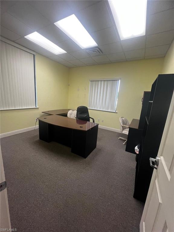 Professional office space featuring recessed ceiling lighting, neutral yellow walls, carpeted flooring, and multiple window treatments providing natural light