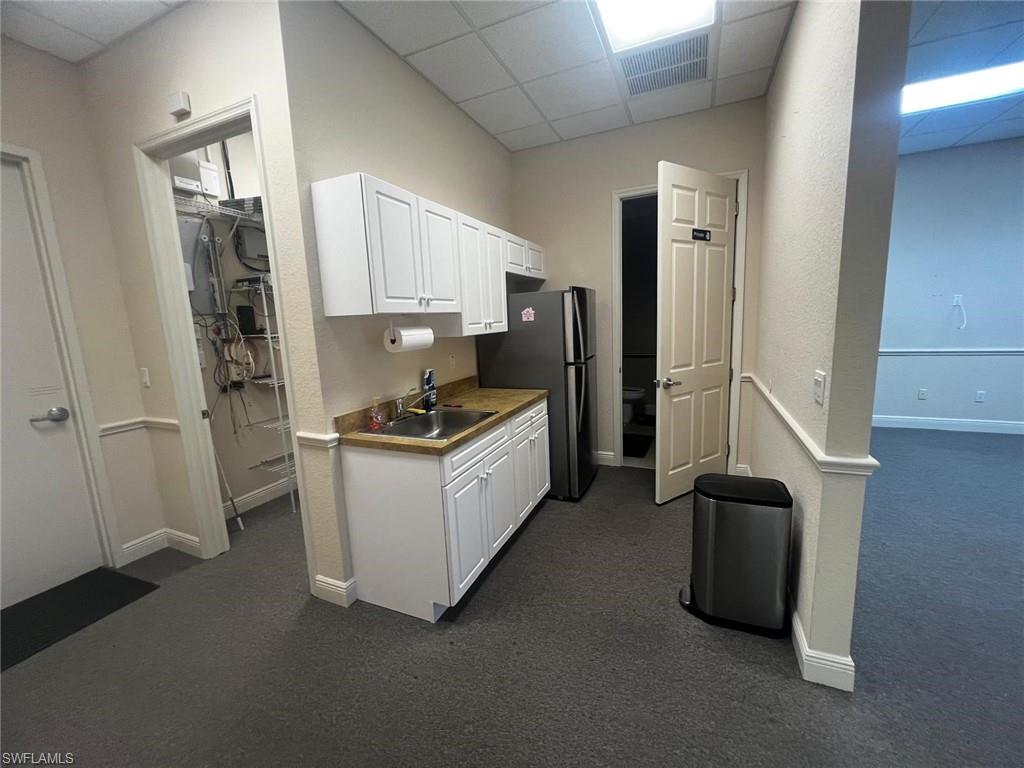 Kitchenette with white cabinetry, stainless steel sink, and light-toned countertop