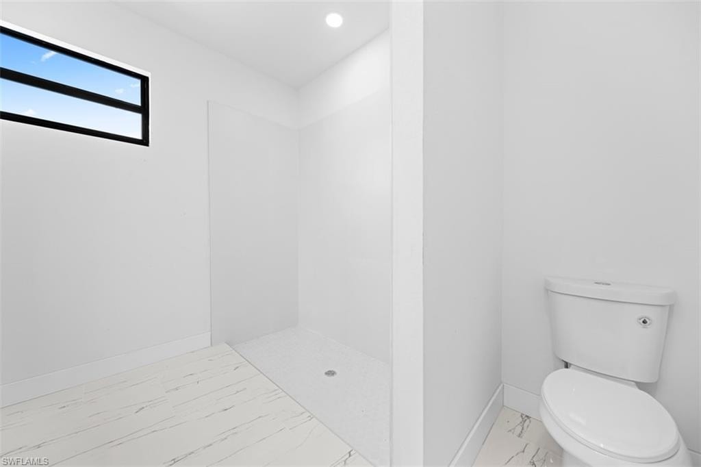 Walk-in shower with a clear glass partition, contemporary black-framed window, recessed ceiling lighting, and white porcelain toilet