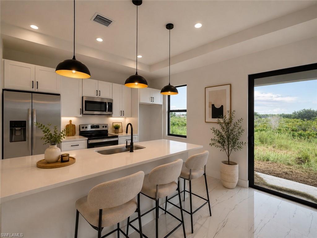 Modern kitchen featuring stainless steel appliances, white cabinetry with brushed nickel hardware, quartz countertops, and a waterfall-edge island