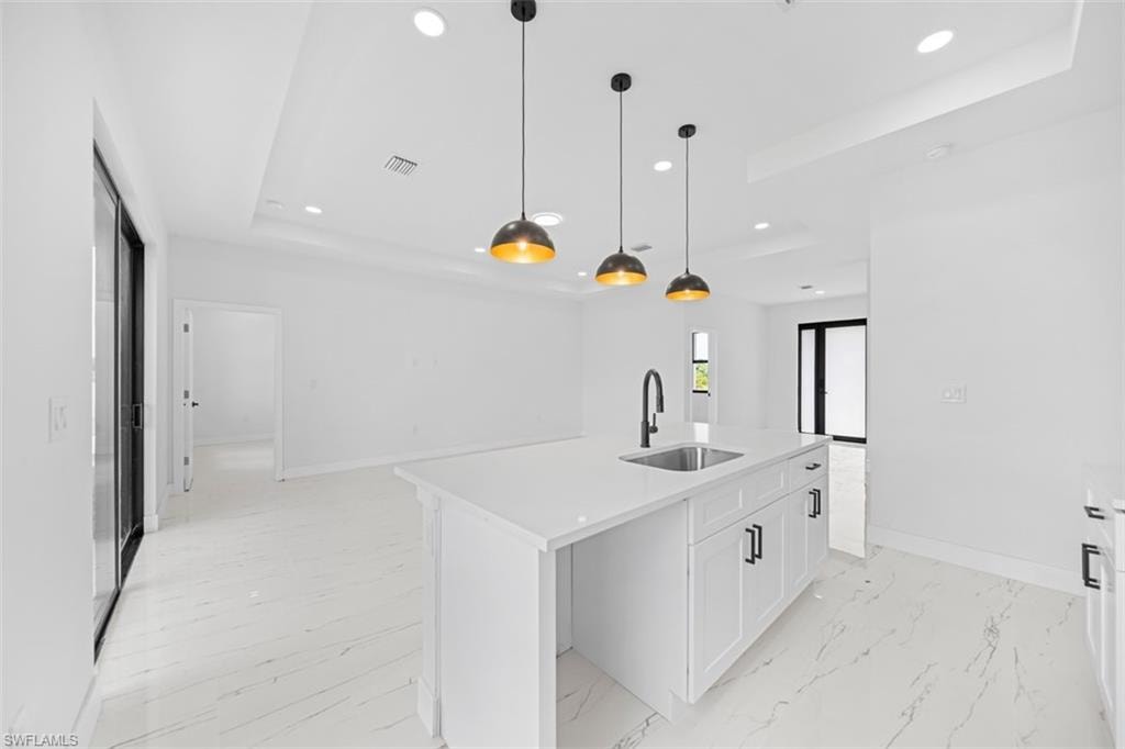 White cabinetry with black hardware, quartz countertop island with undermount sink, three pendant light fixtures, and white tile flooring