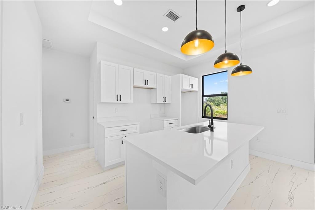 Kitchen featuring white cabinetry, a central island with an undermount sink, pendant lighting, and light-toned flooring