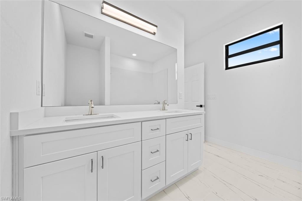 Dual undermount sinks with brushed nickel faucets, expansive vanity mirror, integrated overhead vanity lighting, white shaker-style cabinetry, and light-toned tile flooring