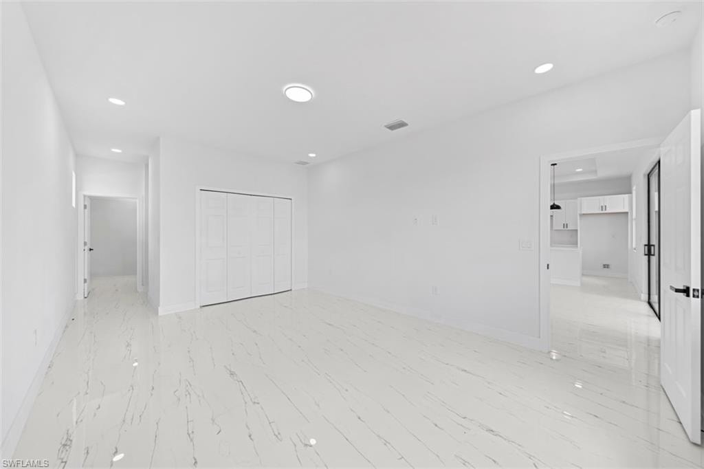 Spacious room featuring white walls, large format tile flooring, recessed lighting, and white bi-fold closet doors