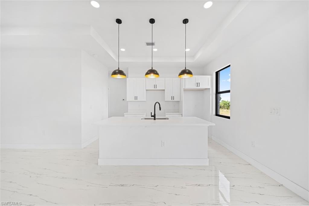 Kitchen featuring an island with an integrated sink, white cabinetry, and three pendant lights