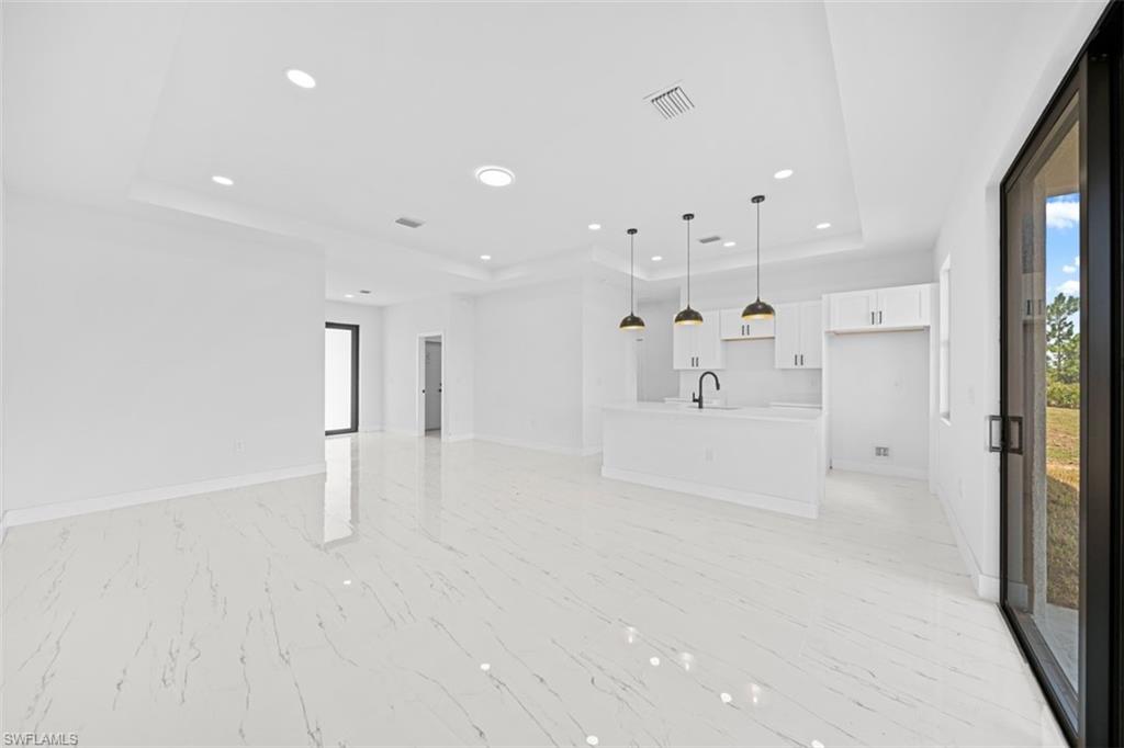 Open-concept interior featuring white-finish cabinetry, a kitchen island with pendant lighting, polished tile flooring, and a tray ceiling with recessed lighting