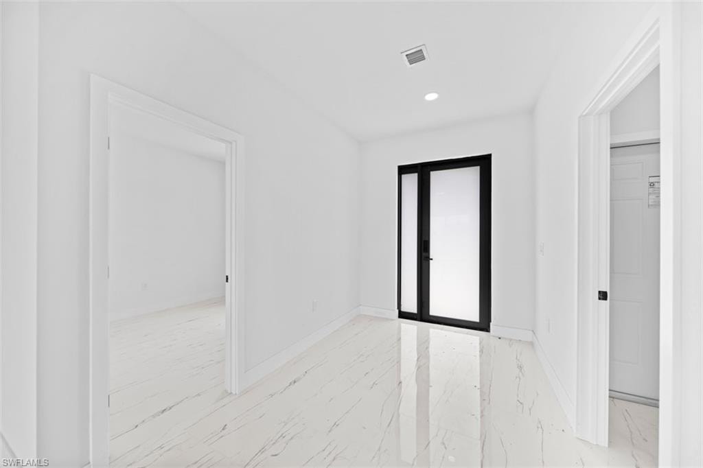 White walls with recessed lighting and a black-framed glass door