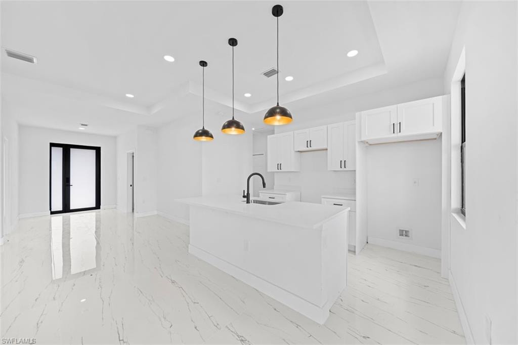 Open-concept kitchen featuring an island with an undermount sink, pendant lighting, white cabinetry, and white tile flooring