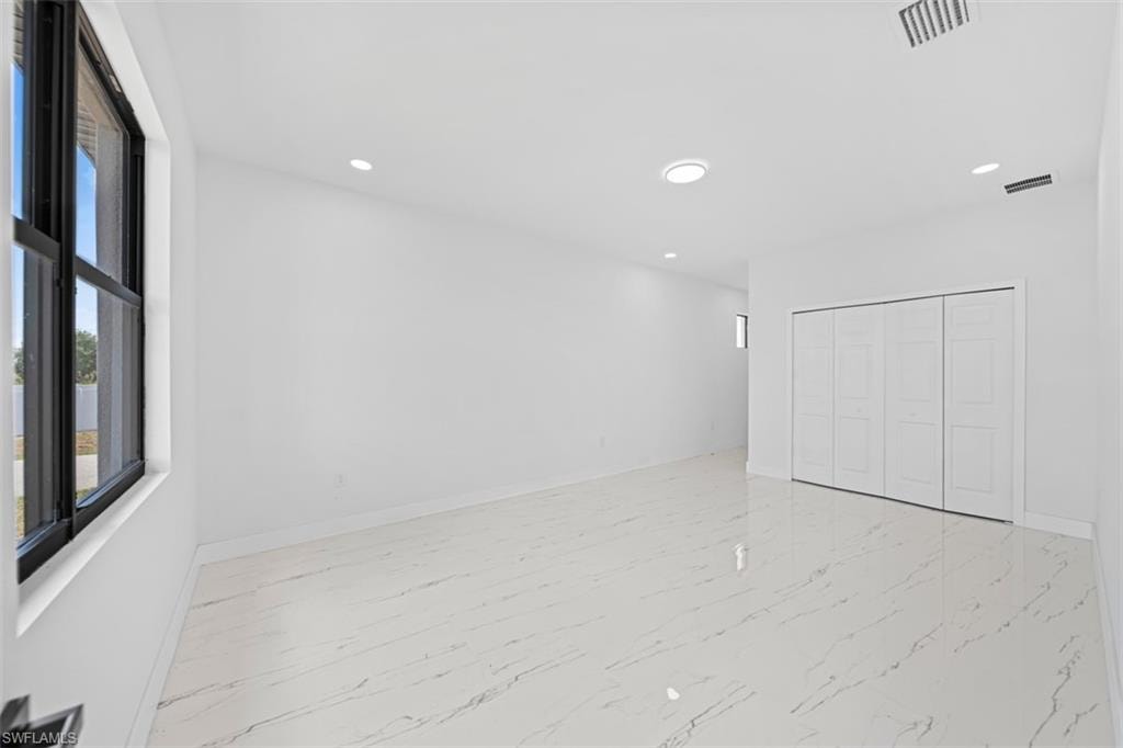 Spacious interior with white walls, large format tile flooring, black-framed window, and recessed lighting