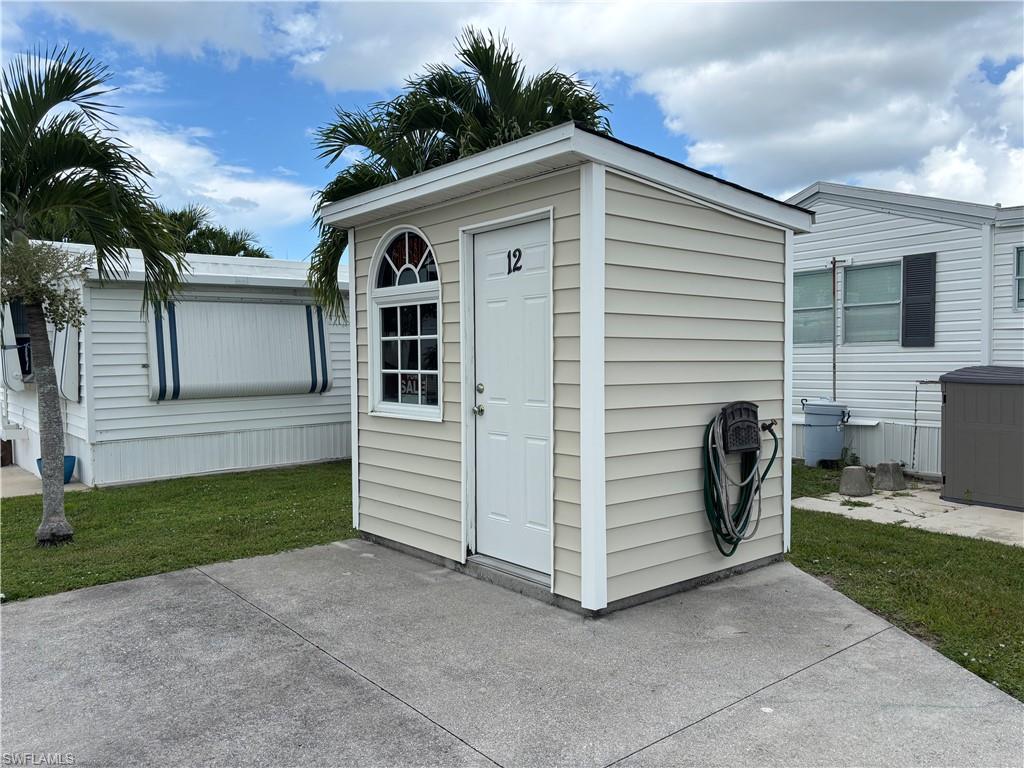 Storage shed with light-toned siding, white trim, and a white entry door