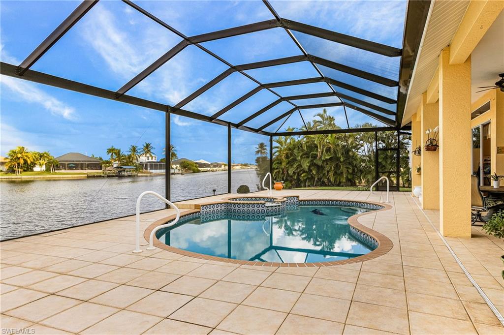 View of pool featuring glass enclosure, a sunroom, a water view, a patio area, and a pool with connected hot tub