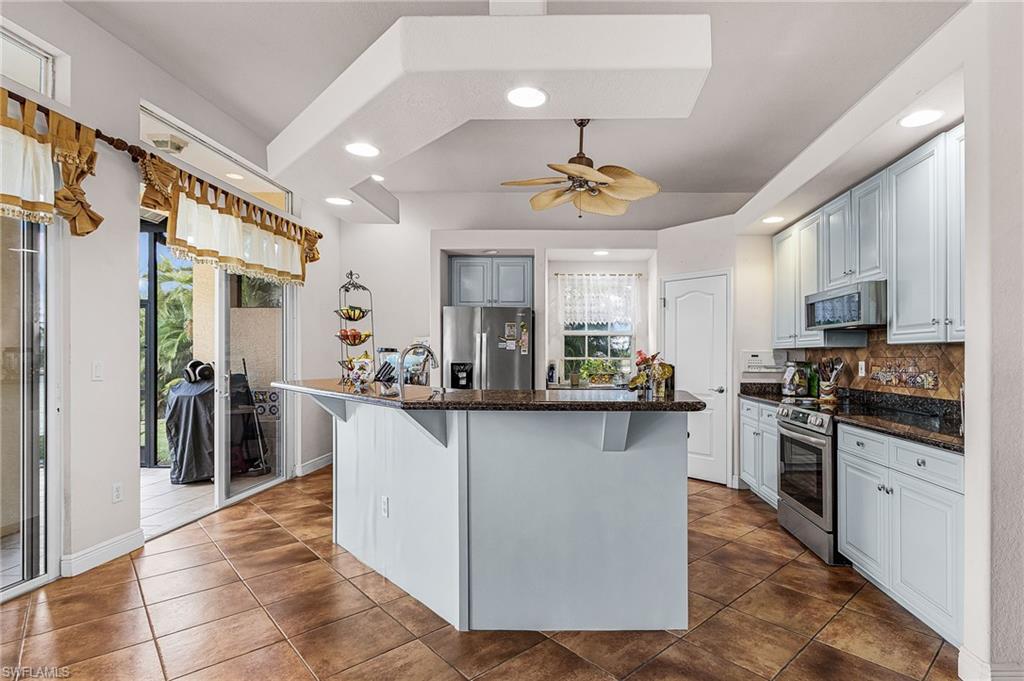 Kitchen featuring a kitchen breakfast bar, dark stone counters, stainless steel appliances, recessed lighting, and a ceiling fan