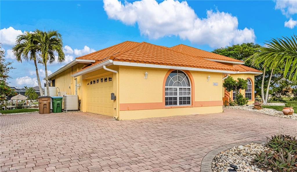 View of side of home with decorative driveway, an attached garage, stucco siding, and a tile roof