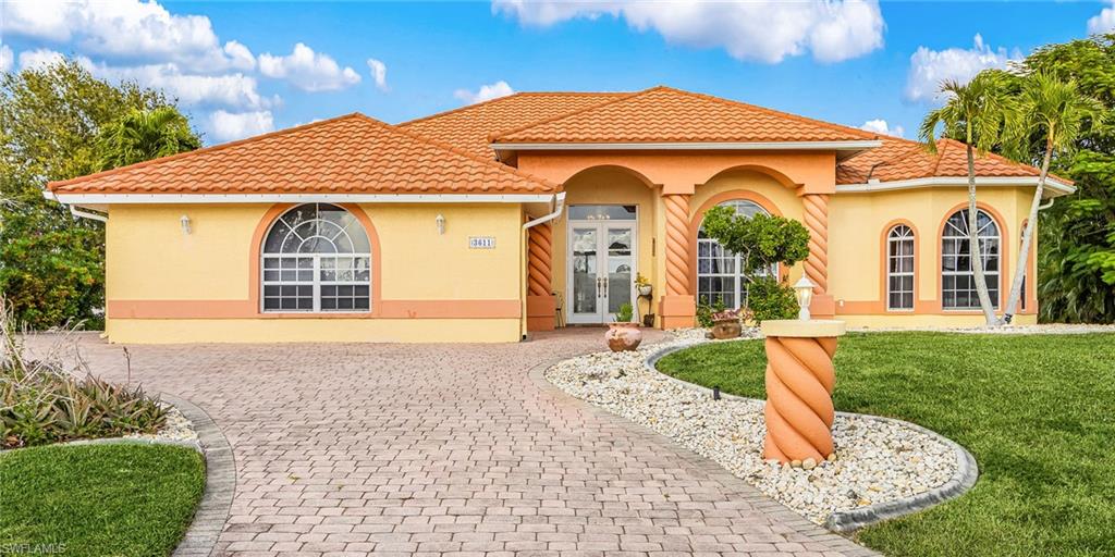 Mediterranean / spanish-style home featuring french doors, a front lawn, stucco siding, and decorative driveway