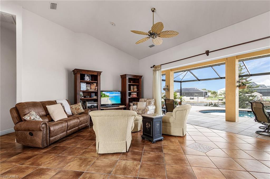 Living room with a sunroom, a ceiling fan, dark tile patterned flooring, and high vaulted ceiling