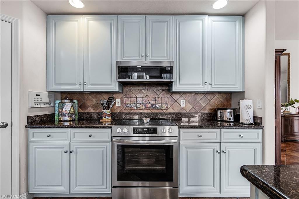 Kitchen featuring appliances with stainless steel finishes, dark stone counters, tasteful backsplash, and white cabinetry