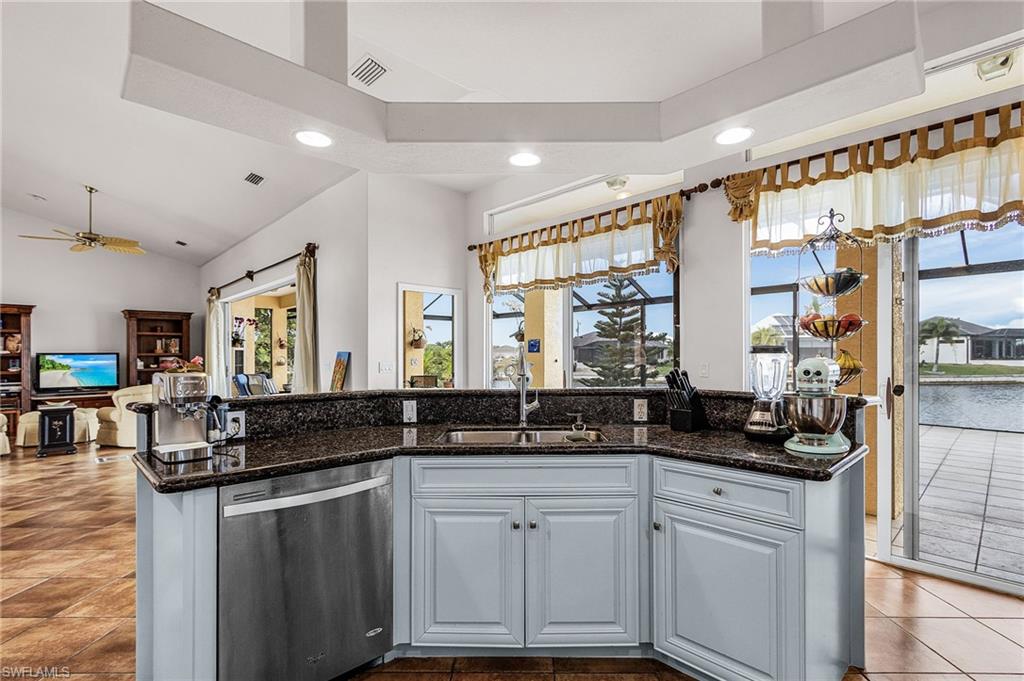 Kitchen featuring dishwasher, white cabinets, a center island with sink, open floor plan, and dark stone counters