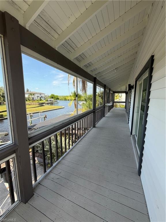 Covered waterfront porch featuring composite decking, black aluminum railings, and expansive windows overlooking the water and surrounding landscape