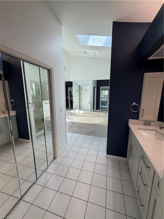 Spa-inspired primary bathroom featuring dual vanities with white cabinetry, tile flooring, and abundant natural light from skylight