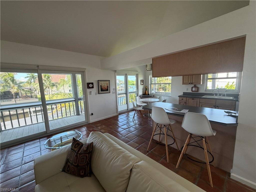 Open-concept living and dining area featuring wood-finish flooring, abundant natural light from expansive glass sliding doors and windows, modern white cabinetry with integrated countertop workspace, and a private balcony accessible from the main living space