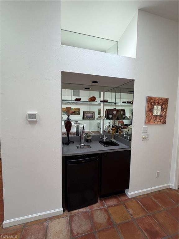 Wet bar featuring dark cabinetry, stainless steel countertop, and mirrored shelving with interior lighting