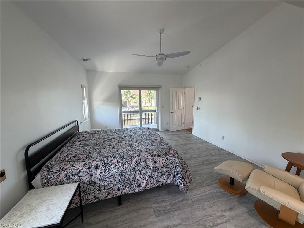 Spacious primary bedroom featuring ceiling fan, wood-finish flooring, glass sliding doors with deck access, and abundant natural light from multiple windows