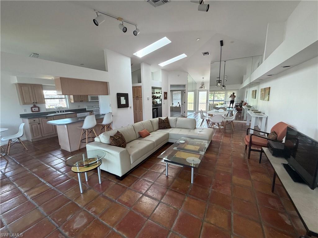 Open-concept living area featuring soaring ceilings with skylights, polished clay tile flooring throughout, and a seamlessly integrated kitchen with wood cabinetry and stainless steel appliances