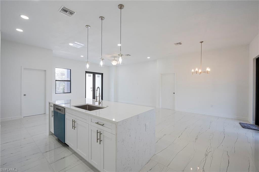 Kitchen with light stone countertops, white cabinets, an island with sink, open floor plan, and dishwasher