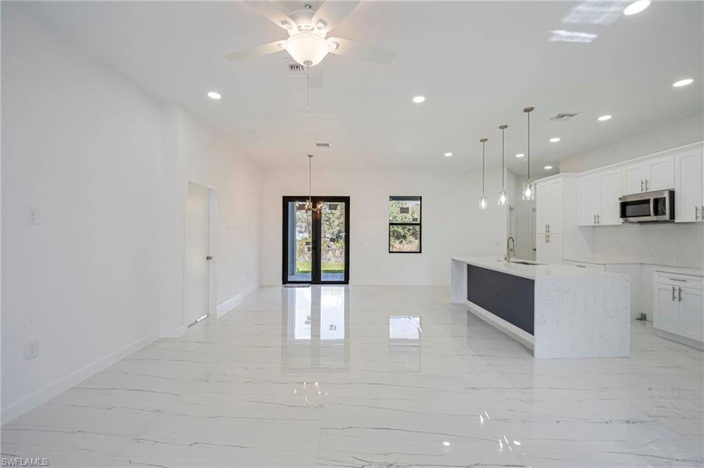 Kitchen with white cabinets, light stone countertops, light marble finish flooring, and a kitchen island with sink
