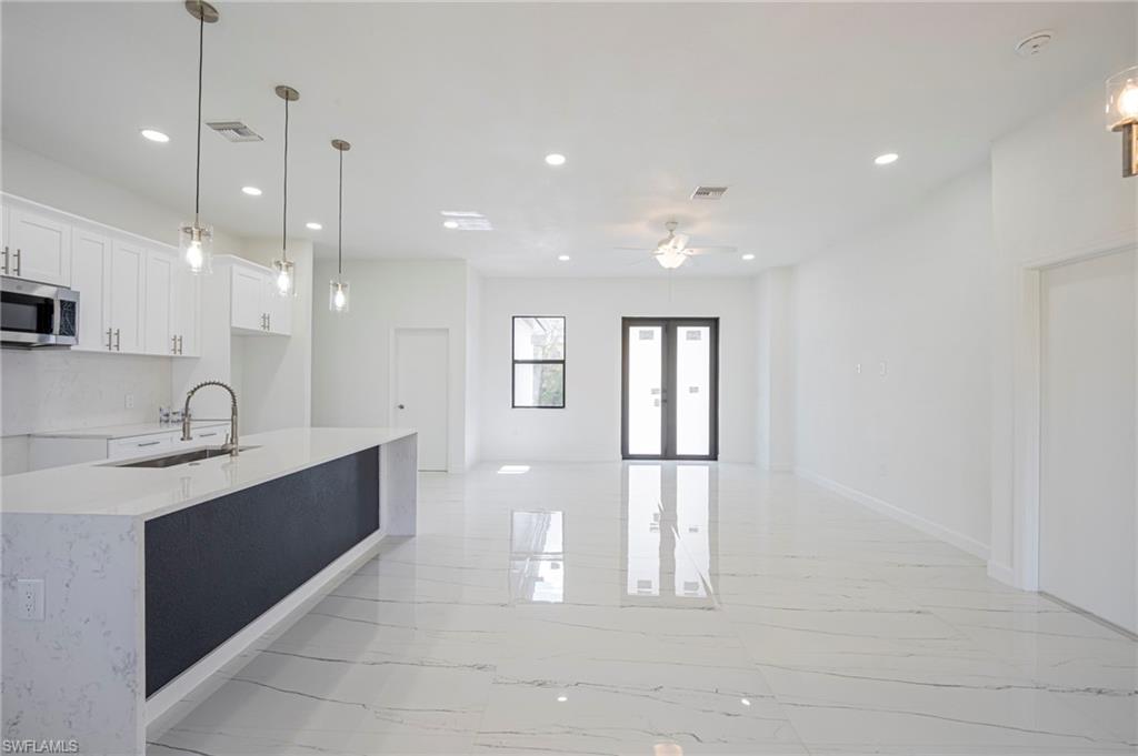 Kitchen featuring decorative light fixtures, light stone counters, stainless steel microwave, white cabinets, and open floor plan