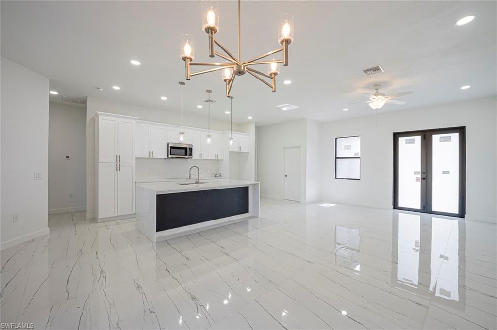Kitchen featuring open floor plan, a chandelier, white cabinets, a kitchen island with sink, and light stone counters