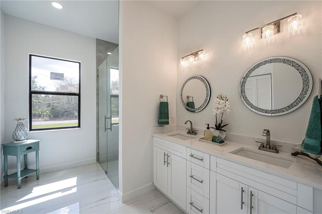 Bathroom featuring double vanity, a stall shower, and light marble finish flooring