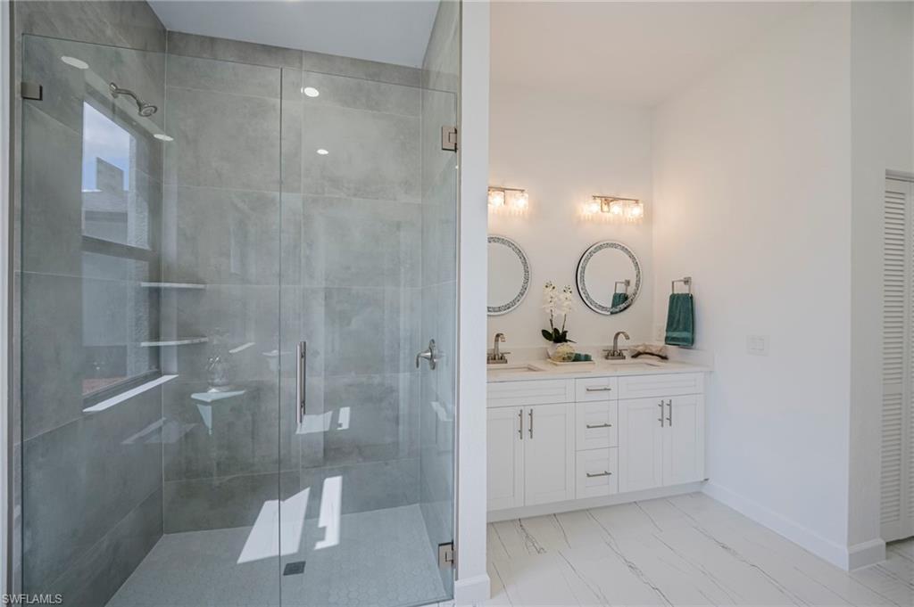 Full bath with double vanity, a shower stall, and a closet