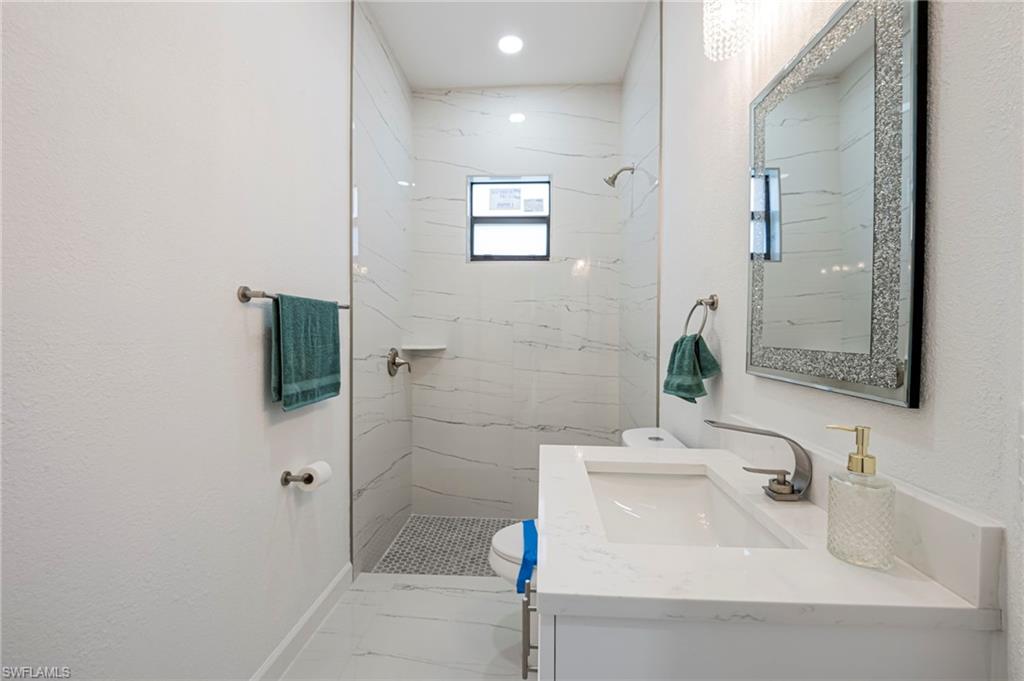 Full bath featuring vanity, a marble finish shower, and a textured wall