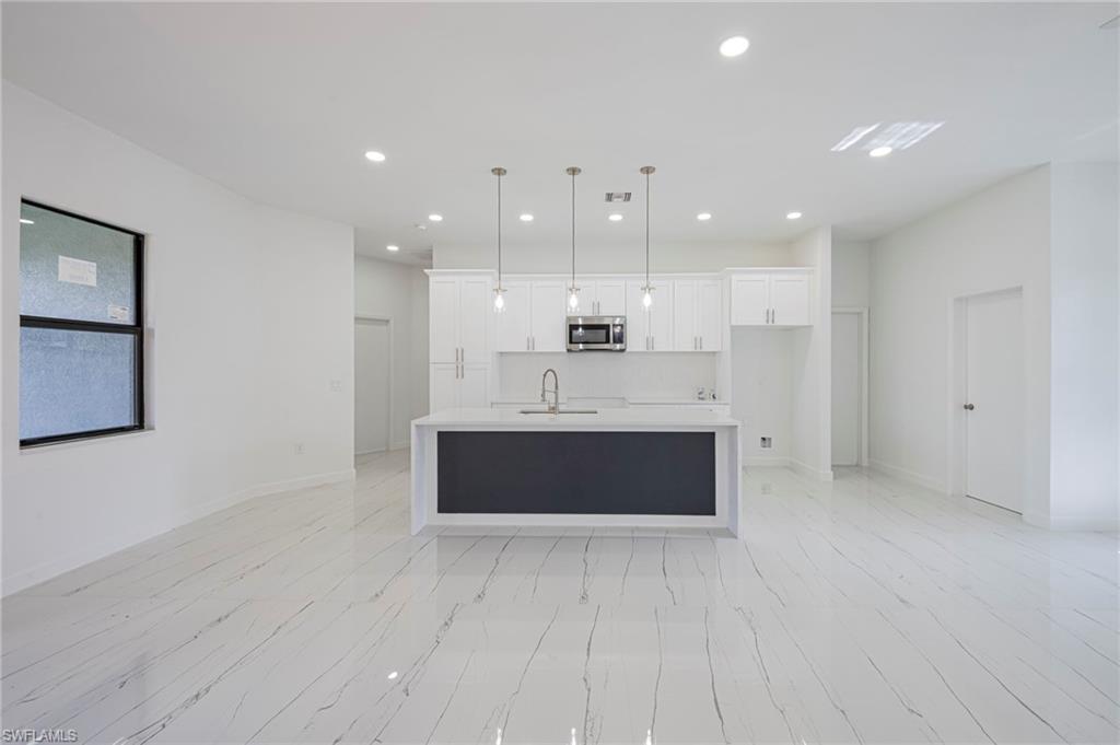Kitchen with decorative light fixtures, a center island with sink, white cabinetry, stainless steel microwave, and light stone counters