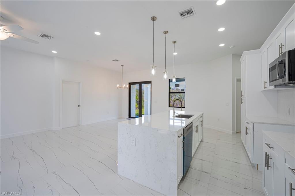 Kitchen with light stone countertops, white cabinets, ceiling fan, a kitchen island with sink, and stainless steel appliances