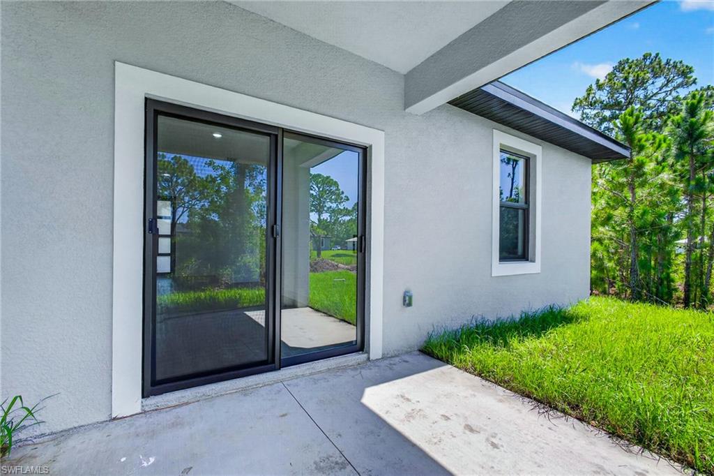 Modern exterior featuring a sliding glass door with black aluminum framing and white trim, concrete patio, and mature landscaping with lush lawn and established trees