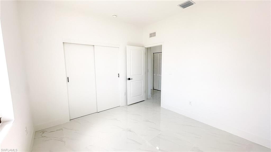 Bright, open bedroom featuring polished concrete flooring, multiple closet spaces with sliding door hardware, and clean white wall finishes throughout