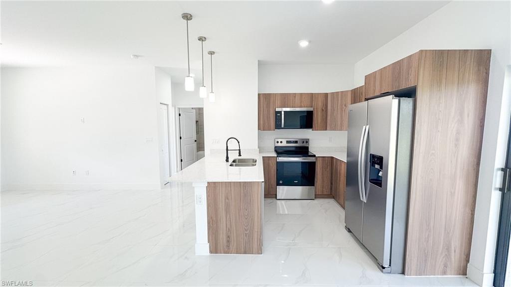 Modern kitchen featuring stainless steel appliances, wood-finish cabinetry, a central island with pendant lighting, white quartz countertops, and white tile flooring throughout the open layout