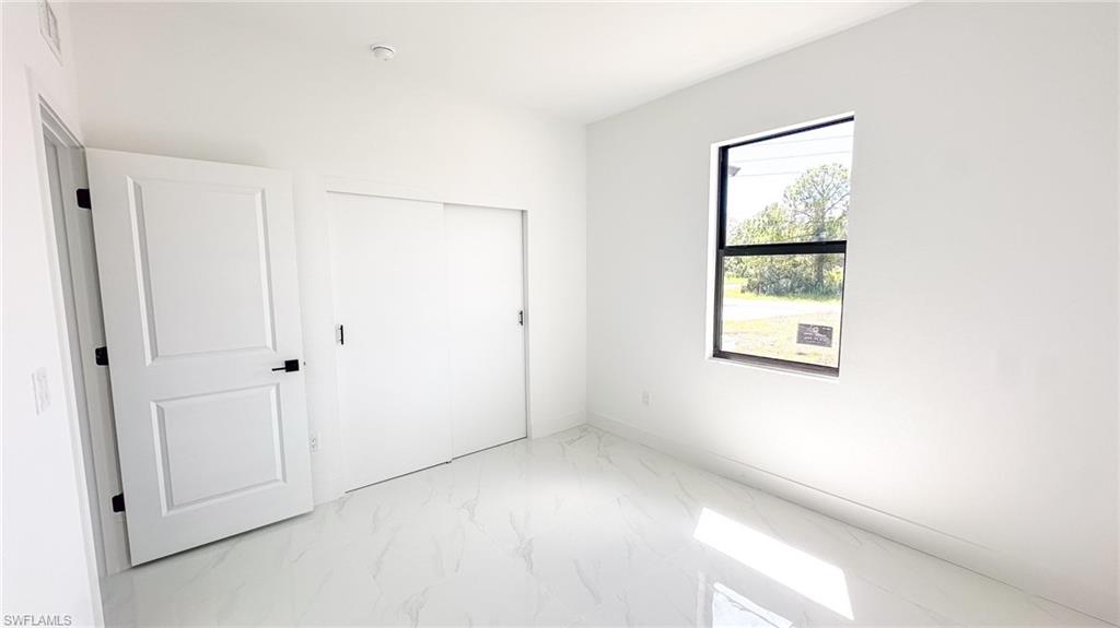 Bright, light-filled bedroom featuring pristine white finishes, sliding closet doors, and a large window framed in black metal
