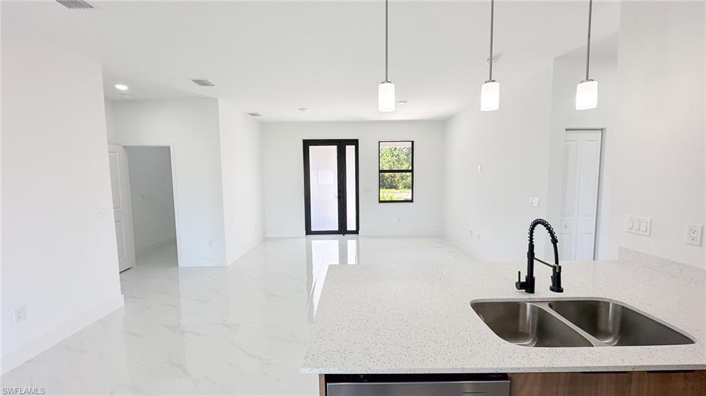 Open-concept kitchen and living area featuring polished light stone flooring, quartz countertops, and a dual-basin stainless steel undermount sink