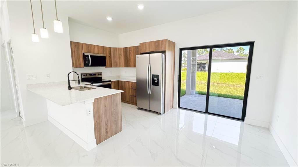 Modern kitchen featuring wood-finish cabinetry, white quartz countertops, a large waterfall-edge island, and stainless steel appliances including a side-by-side refrigerator