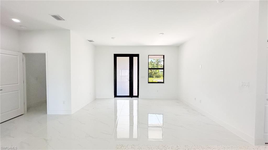 Bright, open interior showcasing polished light-toned flooring throughout, abundant natural light from multiple windows, black-framed glass door entry, and clean white walls with recessed ceiling lighting