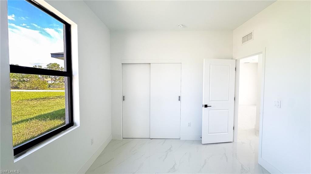 Bright, light-filled bedroom with expansive window framing pastoral grounds, white painted doors with modern hardware, light wood-finish flooring, and clean white wall surfaces throughout