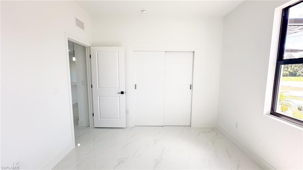 Bright, light-filled bedroom featuring pristine white-finish walls, polished concrete flooring, large picture window with natural light, and sliding closet doors with contemporary hardware