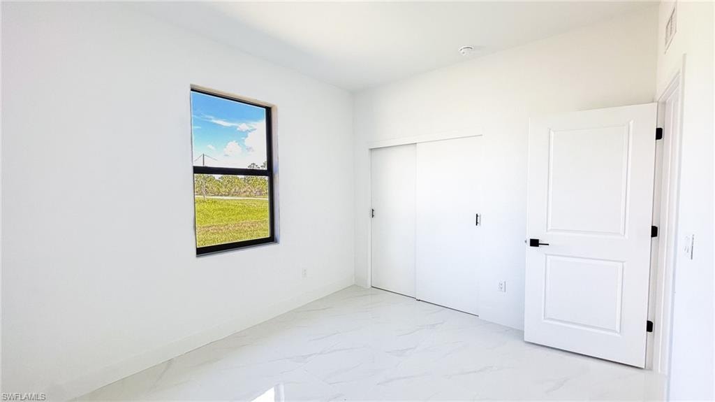 Bright, light-filled bedroom featuring pristine wall-finish surfaces, polished concrete flooring, and dual white panel doors with black hardware