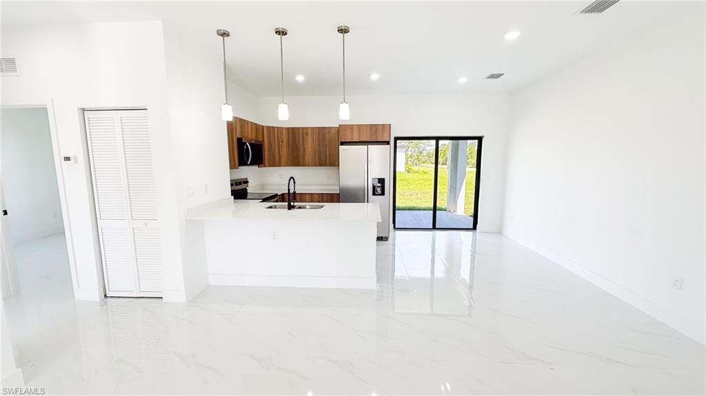 Open-concept living and kitchen area featuring polished concrete flooring, white shiplap walls, wood-finish cabinetry with stainless steel appliances, pendant lighting, and sliding glass doors with black frames providing natural light