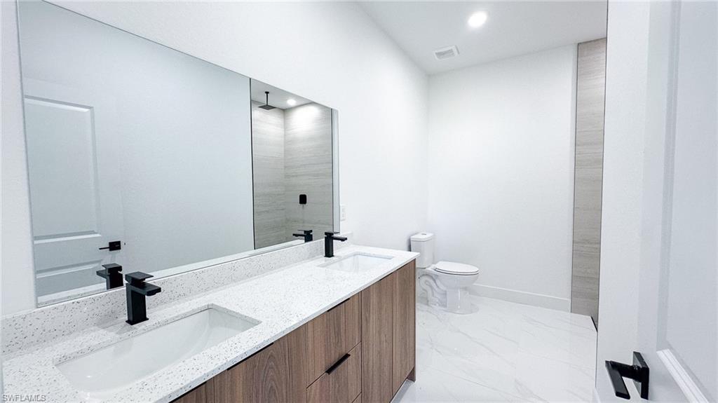 Dual vanity with speckled white countertop, modern wood-finish cabinetry, and matte black fixtures