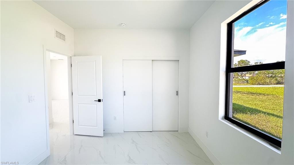 Bright, light-filled bedroom featuring pristine white finish flooring, multiple closet spaces with sliding door hardware, and expansive window framing pastoral landscape views with natural light throughout